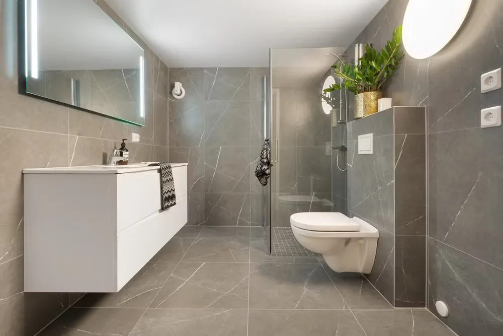 Grey stone-tiled bathroom with a floating white vanity and walk-in shower