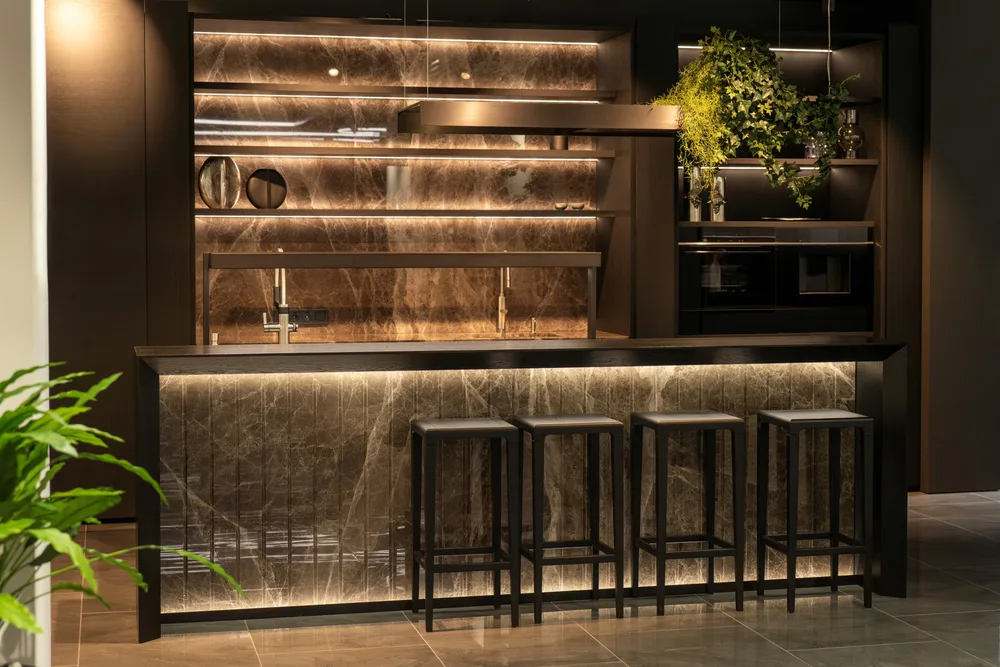 Backlit brown stone bar with shelving and black stools