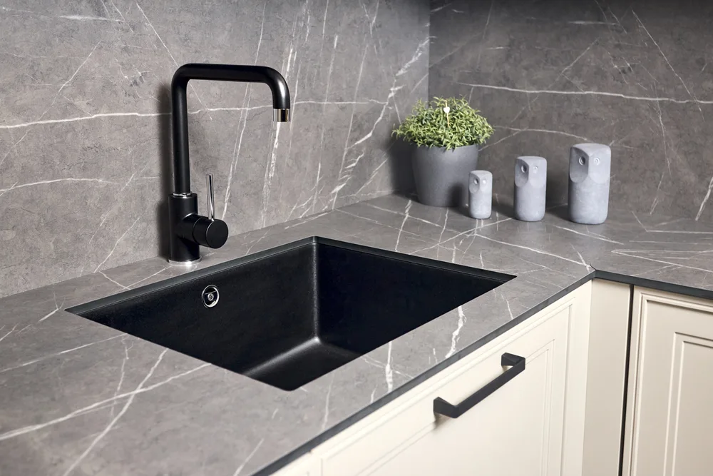 Black undermount sink set into a grey veined stone worktop and splashback